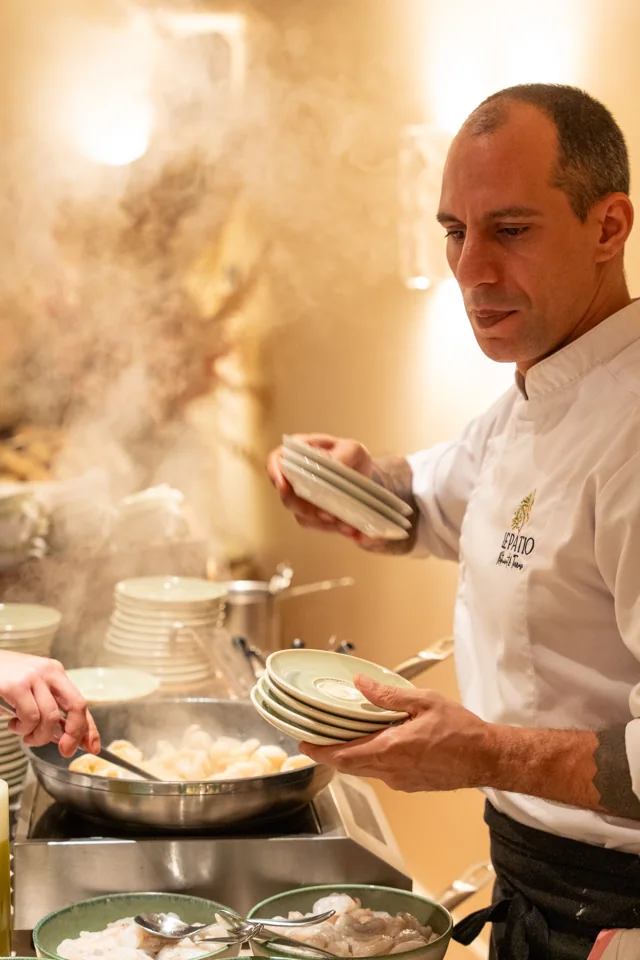 A chef plating food beside a steaming pan during an evening event