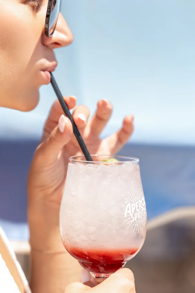 Close-up of a woman enjoying an Aperol-branded cocktail beside the sea
