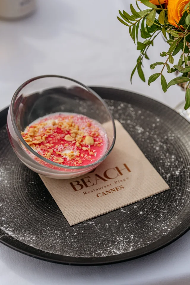 A pink dessert presented in a tilted glass bowl on a restaurant table