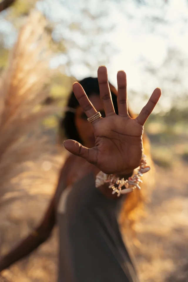 A raised hand displaying rings and bracelets against a softly focused outdoor portrait