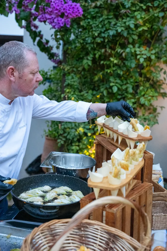 Chef assembling small dishes at an outdoor food station surrounded by greenery