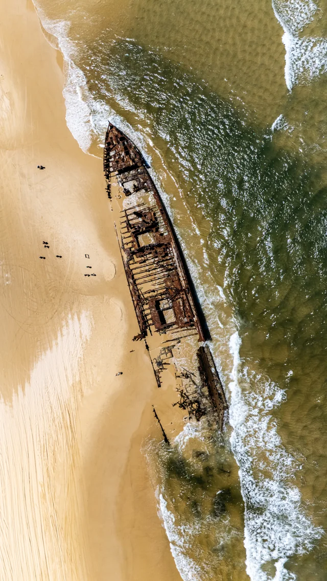 Overhead view of an old wooden shipwreck where waves meet a sandy beach