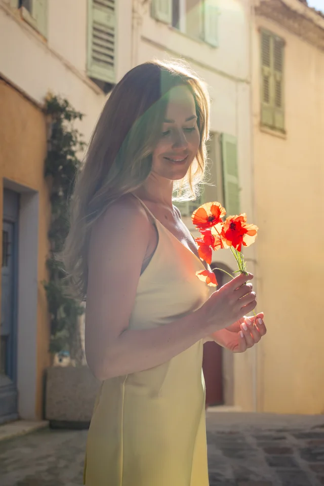 Woman in a pale yellow dress holding red flowers on a sunlit street