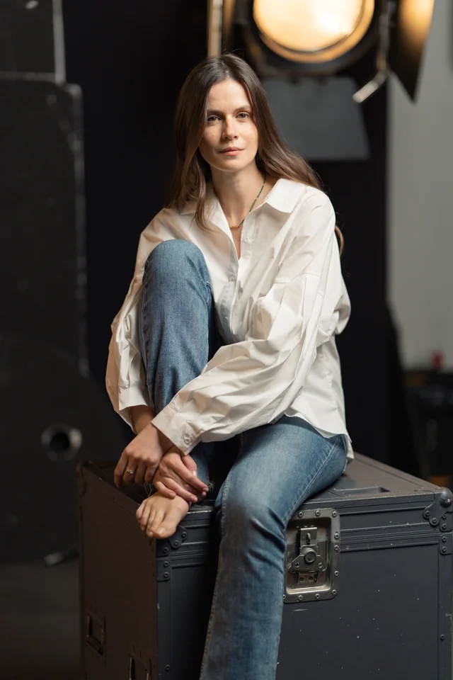 Woman in a white shirt and jeans seated on a studio equipment case