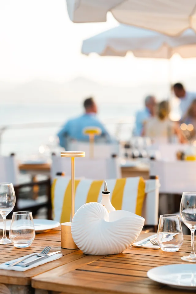 A shell-shaped vase, glassware, and place settings on a sunlit restaurant table